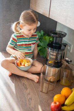 Little girl making fresh juice sitting on the table in home kitchen. High quality photo
