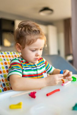 Little girl plays with multi-colored plasticine, creates different shapes. High quality photo