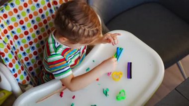 Little girl plays with multi-colored plasticine, creates different shapes. High quality 4k footage