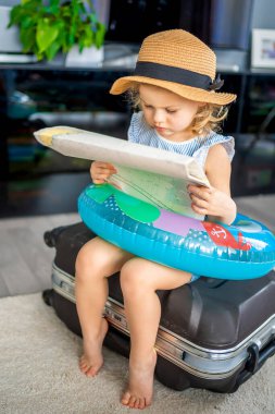 Little girl with suitcase baggage luggage and inflatable life buoy reading map and ready to go for traveling on vacation. High quality photo