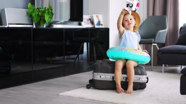 Little girl on suitcase baggage luggage and inflatable life buoy playing with toy plane and ready to go for traveling on vacation. High quality 4k footage