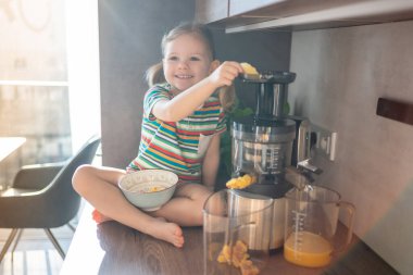 Little girl making fresh juice sitting on the table in home kitchen. High quality photo