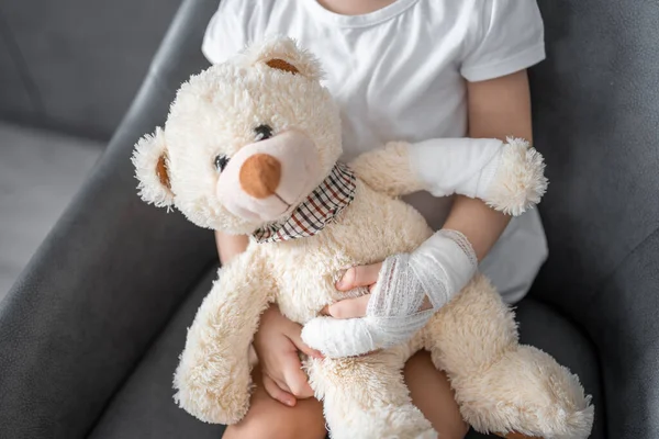 Little girl with broken finger holds teddy bear with a bandaged paw at the doctors appointment in the hospital. High quality photo