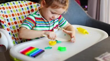 Little girl plays with multi-colored plasticine, creates different shapes with wooden toy knife. High quality 4k footage