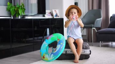 Little girl with suitcase baggage luggage and inflatable life buoy playing with toy camera and ready to go for traveling on vacation. High quality 4k footage