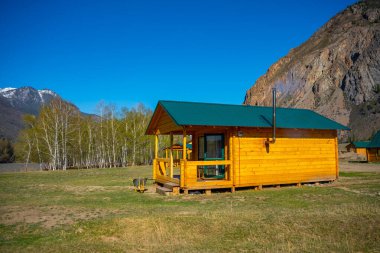 Aktash, Rusya - 8 Mayıs 2022: Aktash kasabası yakınlarındaki Chuya nehrinin kıyısında ve Rusya 'nın Altai kentinde kar tepeli dağlarda tahta misafir evleri. Yüksek kalite fotoğraf