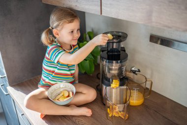 Little girl making fresh juice sitting on the table in home kitchen. High quality photo