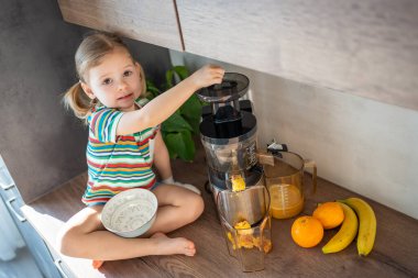Little girl making fresh juice sitting on the table in home kitchen. High quality photo