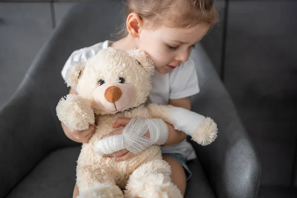 Little girl with broken finger holds teddy bear with a bandaged paw at the doctors appointment in the hospital. High quality photo