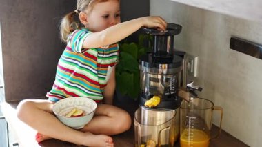 Little girl making fresh juice sitting on the table in home kitchen. High quality 4k footage