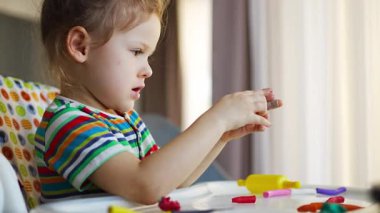 Little girl plays with multi-colored plasticine, creates different shapes. High quality 4k footage