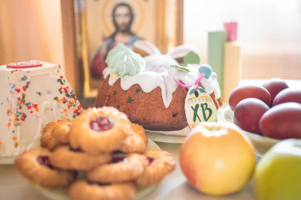Easter cake with painted eggs, apples and cookies on table in home kitchen. Church icons and candle on background. Orthodox religion theme. High quality photo
