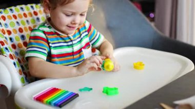 Little girl plays with multi-colored plasticine, creates different shapes with toy rolling pin. High quality 4k footage