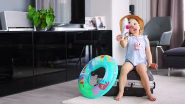 Little girl on suitcase baggage luggage and inflatable life buoy playing with toy plane and ready to go for traveling on vacation. High quality 4k footage