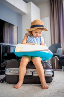 Little girl with suitcase baggage luggage and inflatable life buoy reading map and ready to go for traveling on vacation. High quality photo