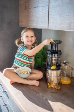 Little girl making fresh juice sitting on the table in home kitchen. High quality photo