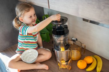 Little girl making fresh juice sitting on the table in home kitchen. High quality photo