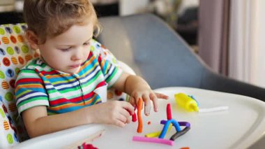 Little girl plays with multi-colored plasticine, creates different shapes. High quality 4k footage