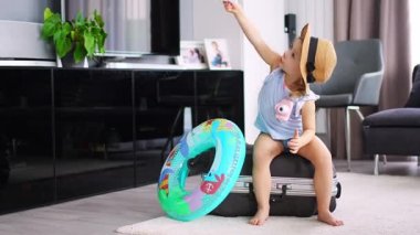 Little girl on suitcase baggage luggage and inflatable life buoy playing with toy plane and ready to go for traveling on vacation. High quality 4k footage
