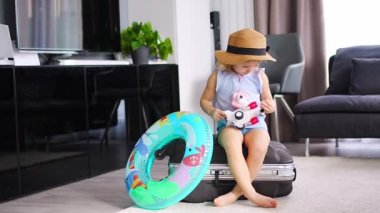 Little girl on suitcase baggage luggage and inflatable life buoy playing with toy plane and ready to go for traveling on vacation. High quality 4k footage