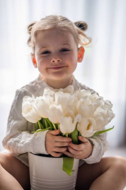 Lale çiçeği buketiyle pencerenin kenarında oturan küçük kız. Mutlu çocuk, içeride. Anneler günü, sevgililer günü ya da doğum günü konsepti. Yüksek kalite fotoğraf