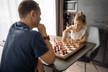 Küçük kız babasıyla ev mutfağında satranç oynuyor. Erken çocukluk gelişimi ve eğitim kavramı. Aile eğlencesi, iletişim ve eğlence. Yüksek kalite fotoğraf