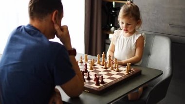Küçük kız babasıyla ev mutfağında satranç oynuyor. Erken çocukluk gelişimi ve eğitim kavramı. Aile eğlencesi, iletişim ve eğlence. Yüksek kalite 4k görüntü