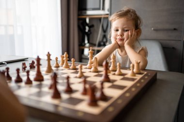 Küçük kız babasıyla ev mutfağında satranç oynuyor. Erken çocukluk gelişimi ve eğitim kavramı. Aile eğlencesi, iletişim ve eğlence. Yüksek kalite fotoğraf