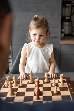 Küçük kız babasıyla ev mutfağında satranç oynuyor. Erken çocukluk gelişimi ve eğitim kavramı. Aile eğlencesi, iletişim ve eğlence. Yüksek kalite fotoğraf