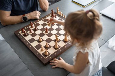 Küçük kız babasıyla ev mutfağında satranç oynuyor. Erken çocukluk gelişimi ve eğitim kavramı. Aile eğlencesi, iletişim ve eğlence. Yüksek kalite fotoğraf