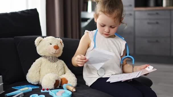 小女孩在家里客厅的沙发上玩医生玩具和玩具熊的游戏 高质量的照片 — 图库视频影像