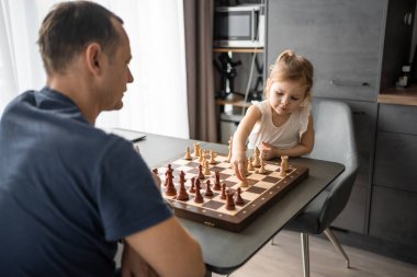 Küçük kız babasıyla ev mutfağında satranç oynuyor. Erken çocukluk gelişimi ve eğitim kavramı. Aile eğlencesi, iletişim ve eğlence. Yüksek kalite fotoğraf