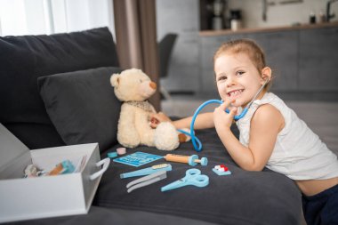 Evdeki oturma odasında kanepede doktorculuk oynayan küçük bir kız. Yüksek kalite fotoğraf