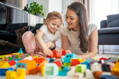 Küçük kız evde anne ya da kadın bebek bakıcısıyla evde inşaat oyuncağıyla oynuyor, eğitim oyunu oynuyor, aile evde boş zamanlarını birlikte geçiriyor. Yüksek kalite fotoğraf