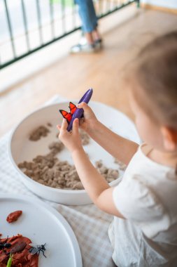 Küçük kız kinetik kum ve oyuncak böcekleriyle oynuyor. Duyusal gelişim ve deneyimler, çocuklarla ilgili temalı aktiviteler, iyi motor beceriler geliştirme. Yüksek kalite fotoğraf