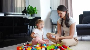 Küçük kız evde anne ya da kadın bebek bakıcısıyla evde inşaat oyuncağıyla oynuyor, eğitim oyunu oynuyor, aile evde boş zamanlarını birlikte geçiriyor. Yüksek kalite 4k görüntü