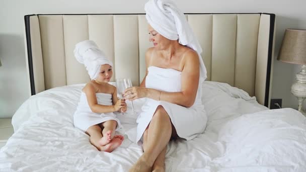 快乐的家庭母亲和小女儿穿着礼服和毛巾 在家里泡温泉的时候笑着用眼镜喝水 高质量的4K镜头 — 图库视频影像