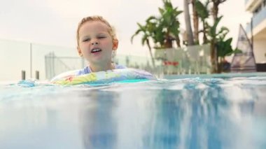 Mutlu küçük kız yazın şişme yüzükle havuzda yüzer. Çocuk, lüks havuzda yüzmeyi öğreniyor. Yüksek kalite 4k görüntü