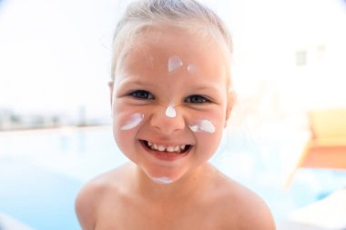 Yüzme havuzunda oynayan, yüzünde güneş kremi olan küçük bir kız. Yaz güneşinde güvenlik. Yüksek kalite fotoğraf