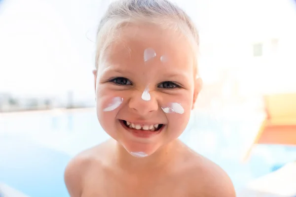 Little girl with sunscreen cream on her face playing at the swimming pool. Safety in summer sun. High quality photo