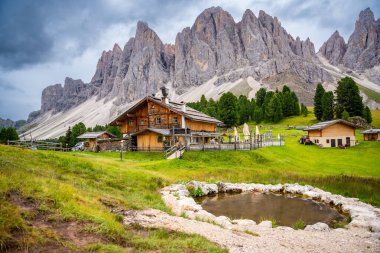 Puez Odle Doğa Parkı 'ndaki Dolomite manzarası. Alp yaylalarından ahşap evler ve yeşil çayırlar görünüyor. Yüksek kalite fotoğraf