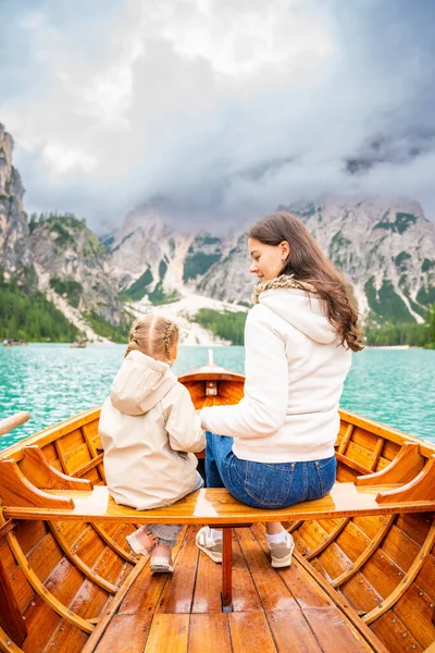 Woman with her daughter sitting in big brown boat at Lago di Braies lake in cloudy day, Italy. Family summer vacation in Europe. High quality photo