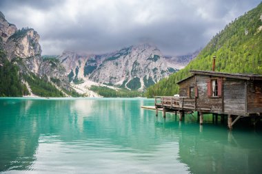 Braies Gölü 'ndeki ahşap ev, İtalya' nın bulutlu bir günde çam ormanları ve Dolomitlerin kayalık dağlarıyla çevrili. Yüksek kalite fotoğraf