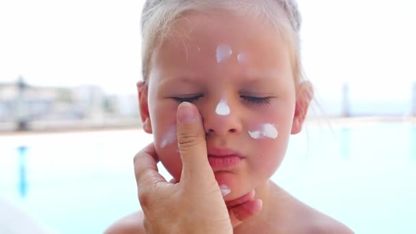 スイミングプールで顔に日焼け止めクリームをかけた小さな女の子 夏の日差しの安全 高品質の4K映像 — ストック動画