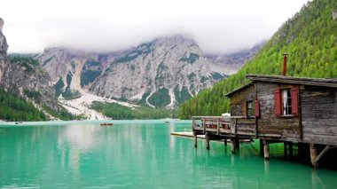 Braies Gölü 'ndeki ahşap ev, İtalya' nın bulutlu bir günde çam ormanları ve Dolomitlerin kayalık dağlarıyla çevrili. Yüksek kalite 4k görüntü