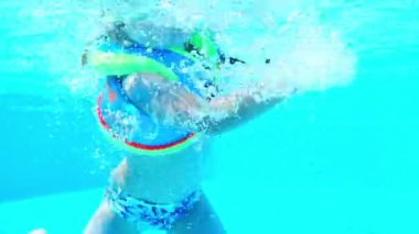 Gözlüklü ve havuzda yelek giymiş su altında yüzen küçük bir kızın portresi. Yaz tatili. Yüksek kalite 4k görüntü
