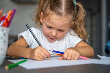 Küçük kız evde renkli kalemlerle resim çiziyor. Yüksek kalite fotoğraf. 