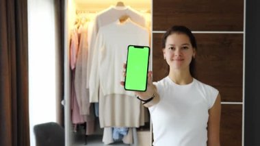 Uygulamada eski istenmeyen kıyafetleri satmak için akıllı telefon uygulaması kullanan genç bir kadın. Krom yeşil ekran. Yüksek kalite 4k görüntü