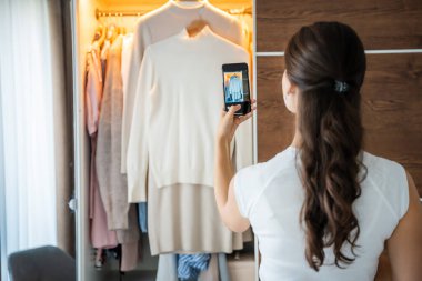 Genç bir kadın, akıllı telefon uygulamasında eski istenmeyen kıyafetlerin fotoğraflarını çekiyor. Yüksek kalite fotoğraf