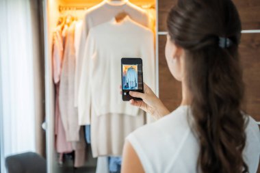 Genç bir kadın, akıllı telefon uygulamasında eski istenmeyen kıyafetlerin fotoğraflarını çekiyor. Yüksek kalite fotoğraf